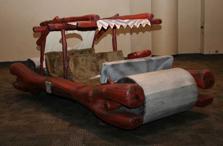 Flintstones car inside, in a poorly-lit room and with a carpet beneath it.