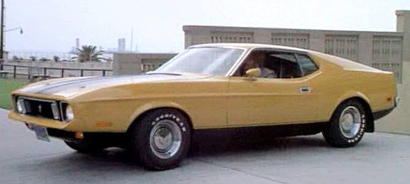 Yellow car with shiny tires in front of some building.