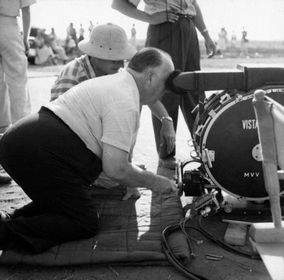 Hitchcock on his knees looking through a camera on the set of North by Northwest.