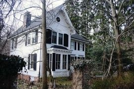 A white house with black curtains surrounded by vegetation